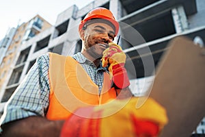 Young construction worker in uniform using walkie talkie on site