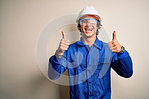 Young constructor man wearing uniform and security helmet over isolated white background success sign doing positive gesture with