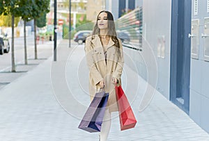 Young content trendy female shopaholic with shopping bags strolling on sidewalk while looking away