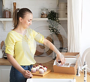 Young cook woman packs cupcakes in a box. Small home business.