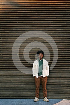 Young cool African American hipster guy standing at wooden wall. Vertical