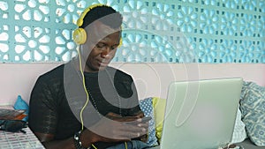 Young cool and attractive black African American hipster man with headphones networking relaxed with mobile phone and laptop