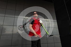 Young cool man hipster posing with electric scooter. Guy in fashionable red- black jeans clothes in sunglasses with a scooter