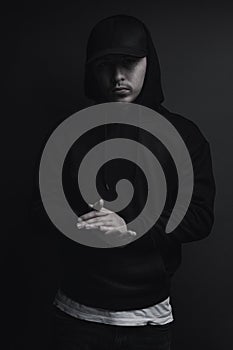 Young cool rapper with black hoodie and cap clap his hands in front of grey background