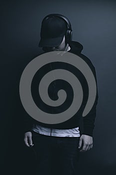 Young cool rapper with black hoodie and cap looking down and listening music