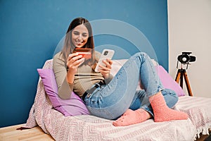 Young coucasian woman smiling using a credit card and a cellphone to order a delivery with a ecommerce app at home. One