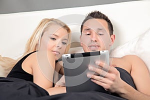 Young coule snuggling in bed with a tablet