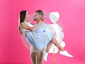 Young couple and air balloons on pink . Celebration of Saint Valentine`s Day