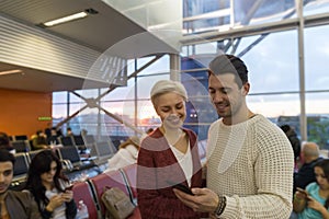 Young Couple In Airport Lounge Waiting Departure Happy Smile Man And Woman Use Cell Smart Phone