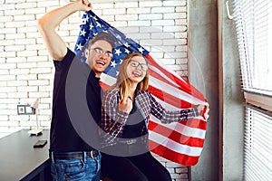 Young couple with an American flag smiling indoors.