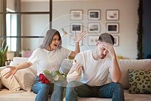 Young couple angry woman and tired handsome man both sitting on the sofa quarrelling on saint valentine`s day, family drama