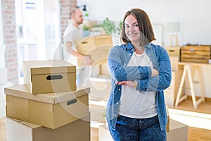 Young couple arround cardboard boxes moving to a new house, plus size woman standing at home happy face smiling with crossed arms