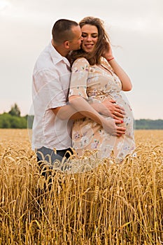 Young couple awaiting baby embrace the field