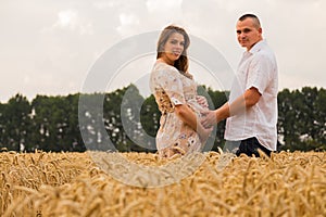 Young couple awaiting baby among the wheat field
