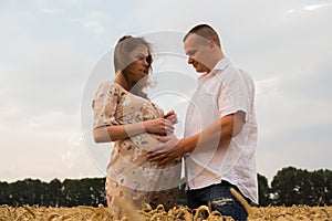 Young couple awaiting baby among the wheat field