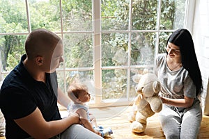 Young couple with a baby playing and sitting on the window sill in a new home