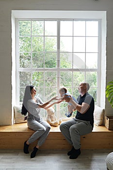 Young couple with a baby playing and sitting on the window sill in a new home