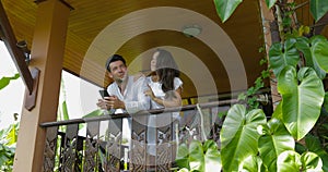 Young couple on balcony looking up talking man and woman embracing hold use cell smart phone happy smiling