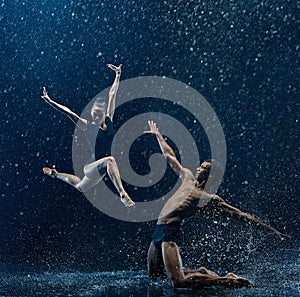 Young couple of ballet dancers dancing unde rwater drops