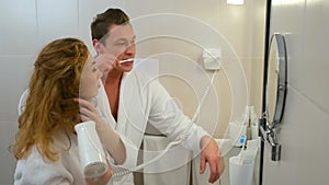 Young couple in bathrobes cleaning teeth together in bathroom before mirror.