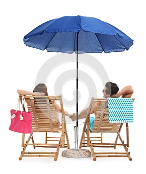 Young couple with beach accessories on sun loungers against white