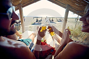 Young couple at beach cheering with drink, laying on sunbeds. Man and woman on vacation, having fun. Holiday, fun, lesiure,