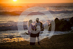 A young couple on the beach embrace during a golden sunset.