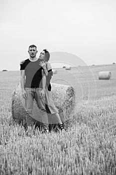 A young couple of beautiful people have fun in the field near round bales of dry hay