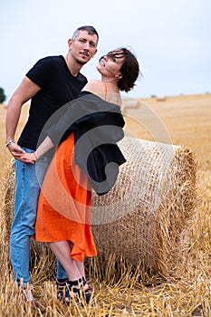 A young couple of beautiful people have fun in the field near round bales of dry hay