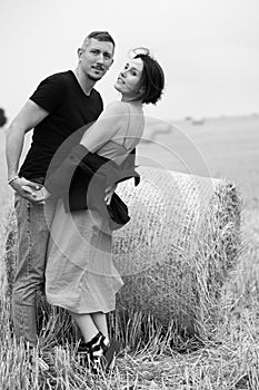 A young couple of beautiful people have fun in the field near round bales of dry hay