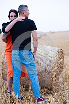A young couple of beautiful people have fun in the field near round bales of dry hay