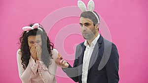 Young couple are beautiful on pink background. During this time they are dressed in rabble ears. Looking at each other