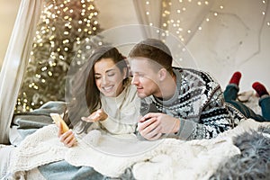 Young couple beautiful woman and handsome man both wearing warm sweaters reading recieved greetings in room decorated for