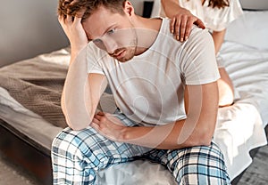 Young couple in the bed. Close-up of unhappy man is sitting on the edge of bed, problem in the bedroom