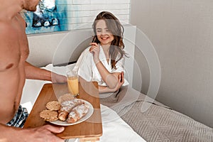 Young couple in the bed. Happy beautiful woman is waking up and ready to eat delicious croissant and juice