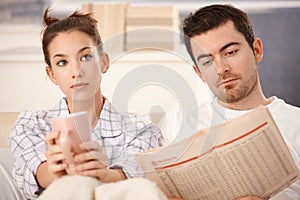 Young couple in bed man reading woman bored