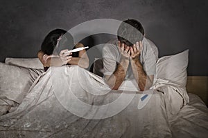 Young couple in bed scared and stressed after positive result on pregnancy test with pregnant woman expecting unwanted baby and ma