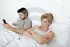 young couple in bed unsatisfied wife frustrated while internet addict husband is using mobile phone social network obsession