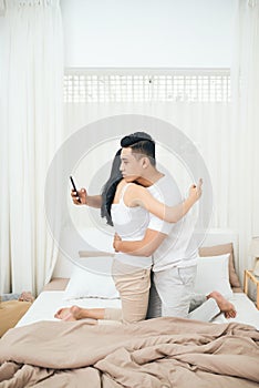 Young couple in the bedroom. Side view of unfaithful man and woman are cheating on the phone while hugging each other