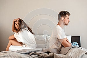 Young couple in the bedroom. Unhappy man and woman are sitting back to back in the bed, couple quarrel home scene