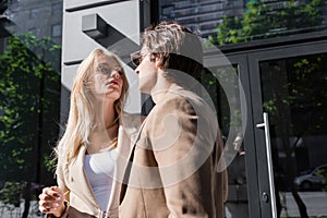 young couple in beige blazers looking at each other on city street,stock image