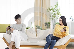 Young couple being in quarrel and not talking.Sitting in living room.Using smartphone