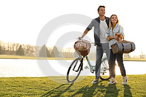 Young couple with bicycle and picnic basket near lake