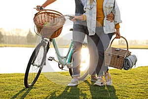 Young couple with bicycle and picnic basket near lake on sunny day