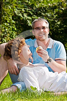 Young couple bites apple, sitting on a grass