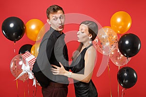 Young couple in black clothes hold gift box celebrating birthday holiday party on bright red background air