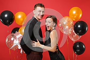 Young couple in black clothes hold gift box celebrating birthday holiday party on bright red background air