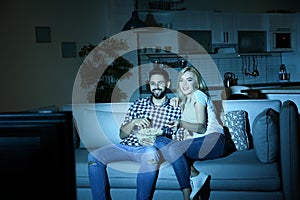 Young couple with bowl of popcorn watching TV on sofa