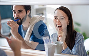 Young couple brushing teeth in front of mirror indoors at home.