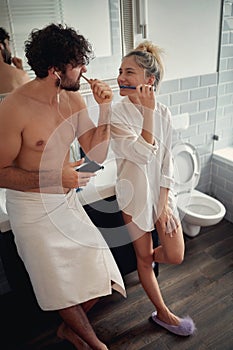 Young couple brushing teeth together in the bathroom, looking each other, smiling, having fun